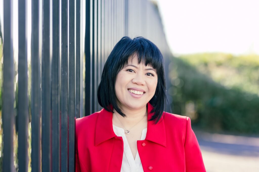Michelle Chow in a red jacket standing beside metal fence